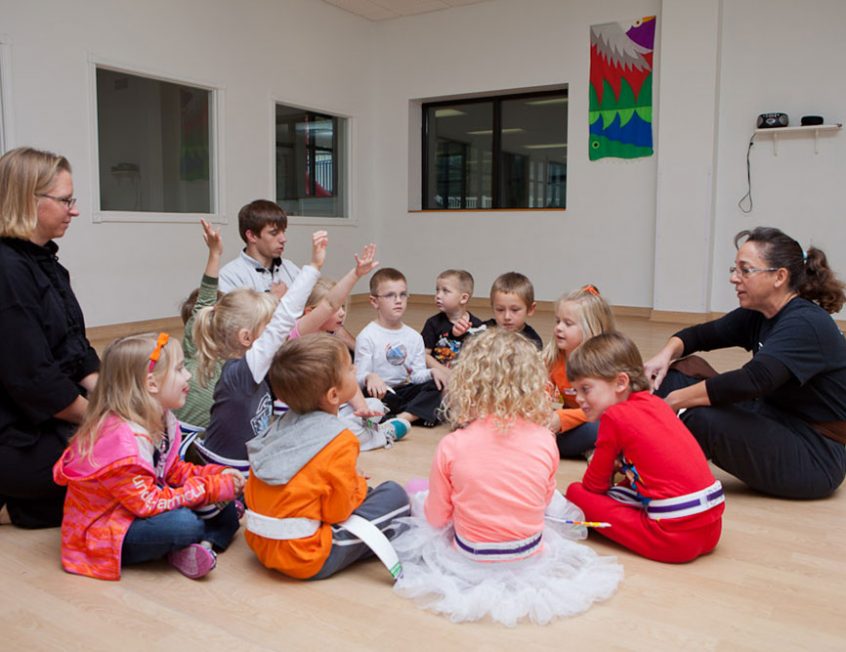 children sitting in a circle raising their hands